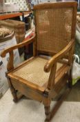 A late Victorian caned and stained beech drop arm commode chair on castors