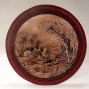 A Continental wall plaque depicting figures on a log within a wood beside cottage on a pink ground,