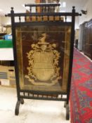 A late Victorian ebonised fire screen in the aesthetic manner with needlework panel of an armorial