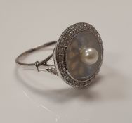 An 18 carat white gold dress ring with mother of pearl disc set with pearl to centre surrounded by