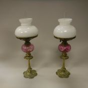 A pair of late Victorian brass candlestick type oil lamps with cranberry glass reservoirs,