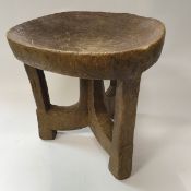 A west African carved wooden stool with circular dished seat on three supports united by centre