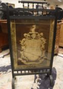 A late Victorian ebonised fire screen in the aesthetic manner with needlework panel of an armorial