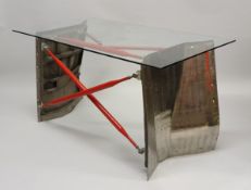 A glass topped desk on metalwork base constructed from two Boeing 747 wing flap sections connected