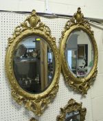 A pair of antique carved giltwood oval mirrors with foliate scroll surmount and basal mount,