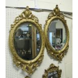 A pair of antique carved giltwood oval mirrors with foliate scroll surmount and basal mount,