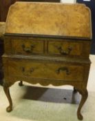 A 1930's burr walnut bureau with sloping fall enclosing an unfitted interior over two short and one