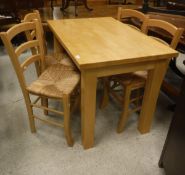 A modern beech kitchen table and four bar-back rush-seated chairs,