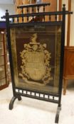 A late Victorian ebonised fire screen in the aesthetic manner with needlework panel of an armorial