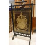 A late Victorian ebonised fire screen in the aesthetic manner with needlework panel of an armorial