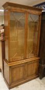 A 20th Century yew wood veneered display cabinet with two glazed doors over two panelled cupboard