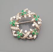 An 18 carat white gold diamond and emerald set circular brooch with foliate design, total weight 7.