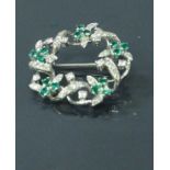 An 18 carat white gold diamond and emerald set circular brooch with foliate design, total weight 7.