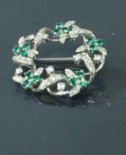 An 18 carat white gold diamond and emerald set circular brooch with foliate design, total weight 7.