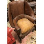 A wing back armchair with brown studded leather and carved front rail