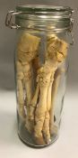 A clear glass jar containing various animal skeletal bone samples including feet,