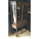 An early 20th Century oak glazed display cabinet with two cupboard doors over two drawers on barley