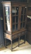 An early 20th Century oak glazed display cabinet with two cupboard doors over two drawers on barley