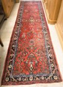 A Persian runner, the central panel set with all-over floral decoration on a red ground,
