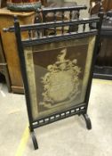 A late Victorian ebonised fire screen in the aesthetic manner with needlework panel of an armorial