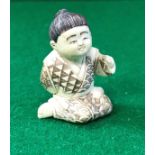 An early 20th Century Chinese carved ivory netsuke as a young kneeling boy bearing script,