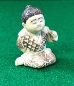 An early 20th Century Chinese carved ivory netsuke as a young kneeling boy bearing script,