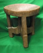 A west African carved wooden stool with circular dished seat on three supports united by centre