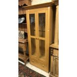 A light oak glass fronted two door display cabinet with four glass shelves