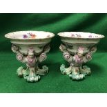 A pair of 19th Century porcelain open salts on figural decorated pedestal bases to scroll feet