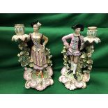 A pair of late 19th/early 20th Century Meissen figural candlesticks with floral encrusted