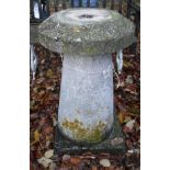 A natural stone staddle stone of conical form on a plinth base