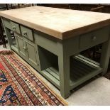 A modern pale green painted kitchen island with multiple drawers and doors and slatted shelving