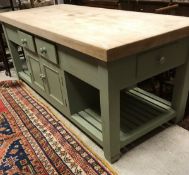 A modern pale green painted kitchen island with multiple drawers and doors and slatted shelving
