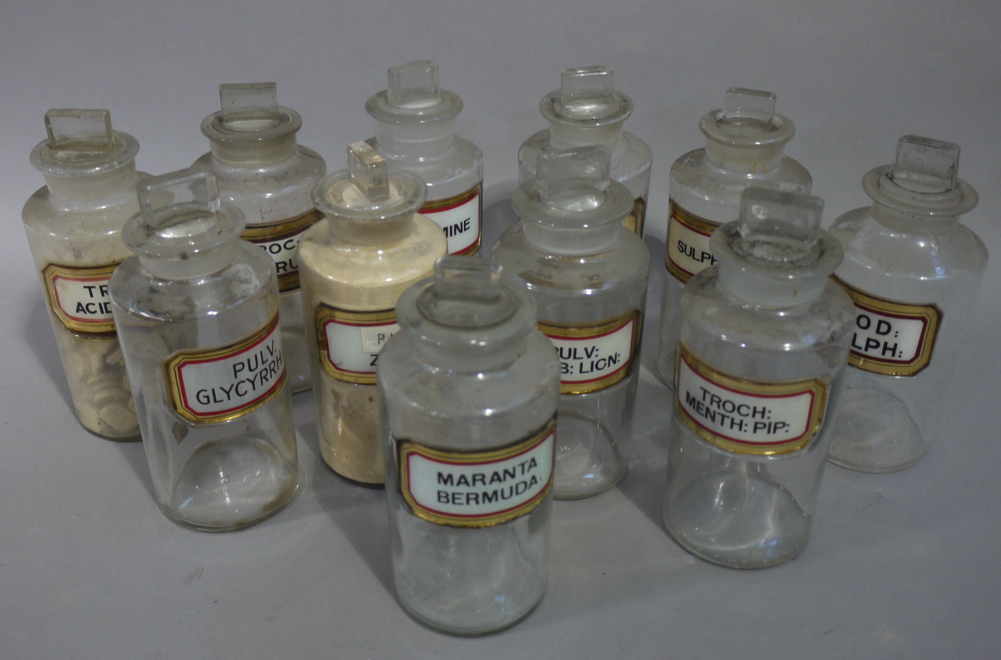 A near set of eleven late 19th/early 20th century clear glass pharmacy bottles, cylindrical,
