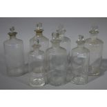 A set of seven clear glass pharmacy bottles, cylindrical, with stoppers, various sizes,