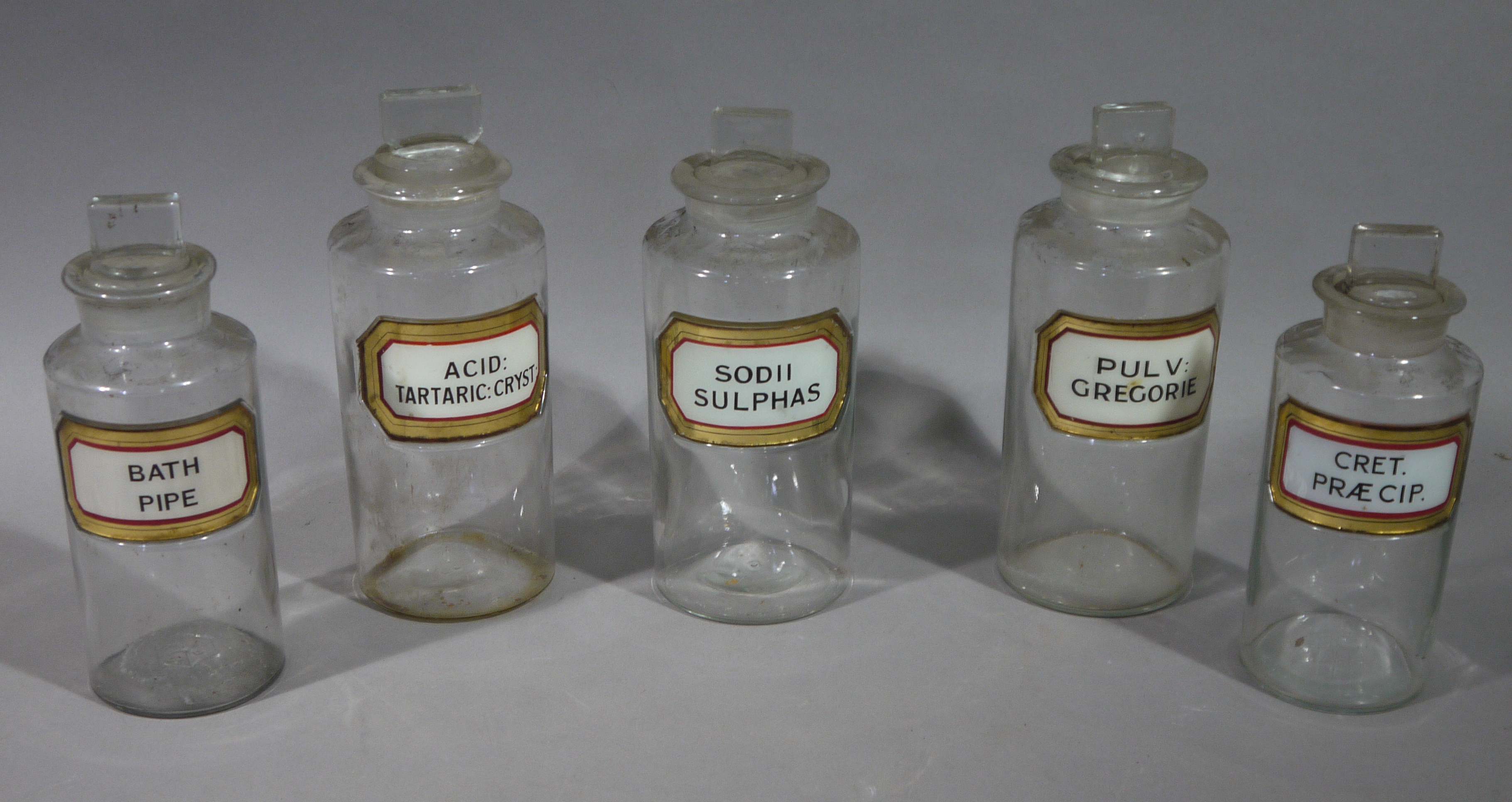 A set of three and a similar pair of late 19th/early 20th century clear glass pharmacy bottles,