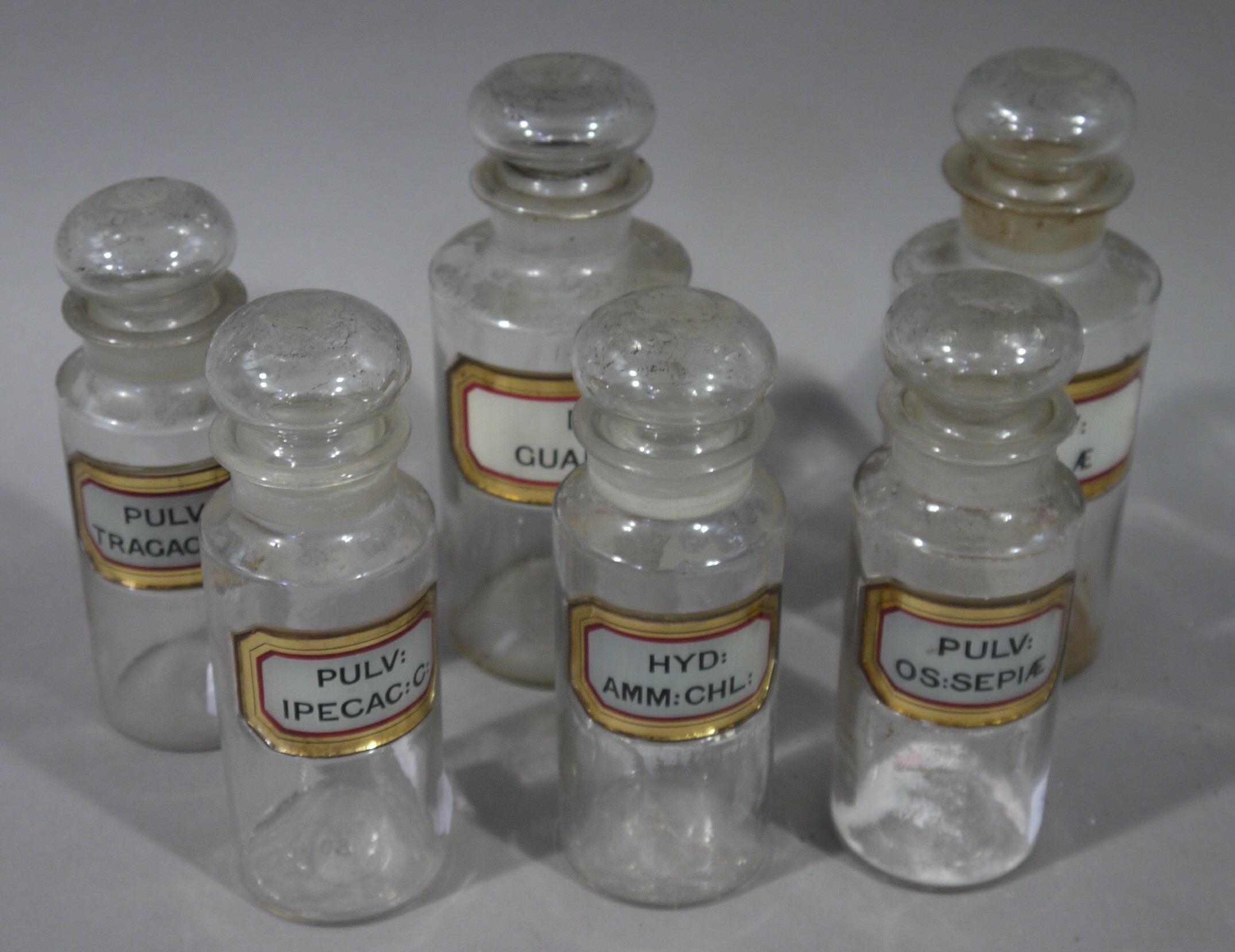 A set of six late 19th/early 20th century clear glass pharmacy bottles in two sizes, cylindrical,