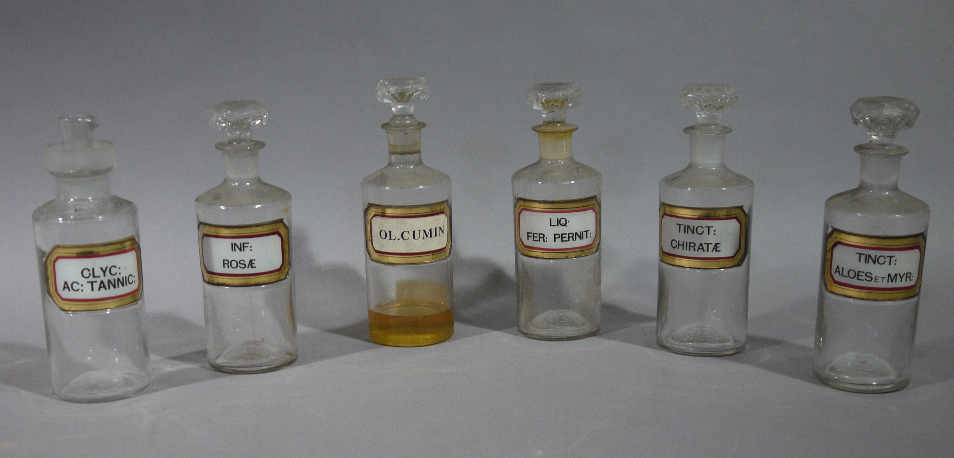 A near set of six late 19th/early 20th century clear glass pharmacy bottles, cylindrical,