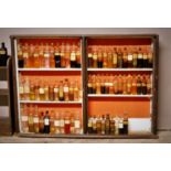 A mahogany framed set of open shelves containing 97 glass flask bottles, with paper labels,