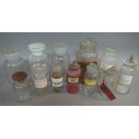 A set of three clear glass pharmacy jars with disc stoppers, another labelled Arneca in black,