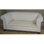 An Edwardian drop end sofa recently upholstered in white and on bun feet with castors