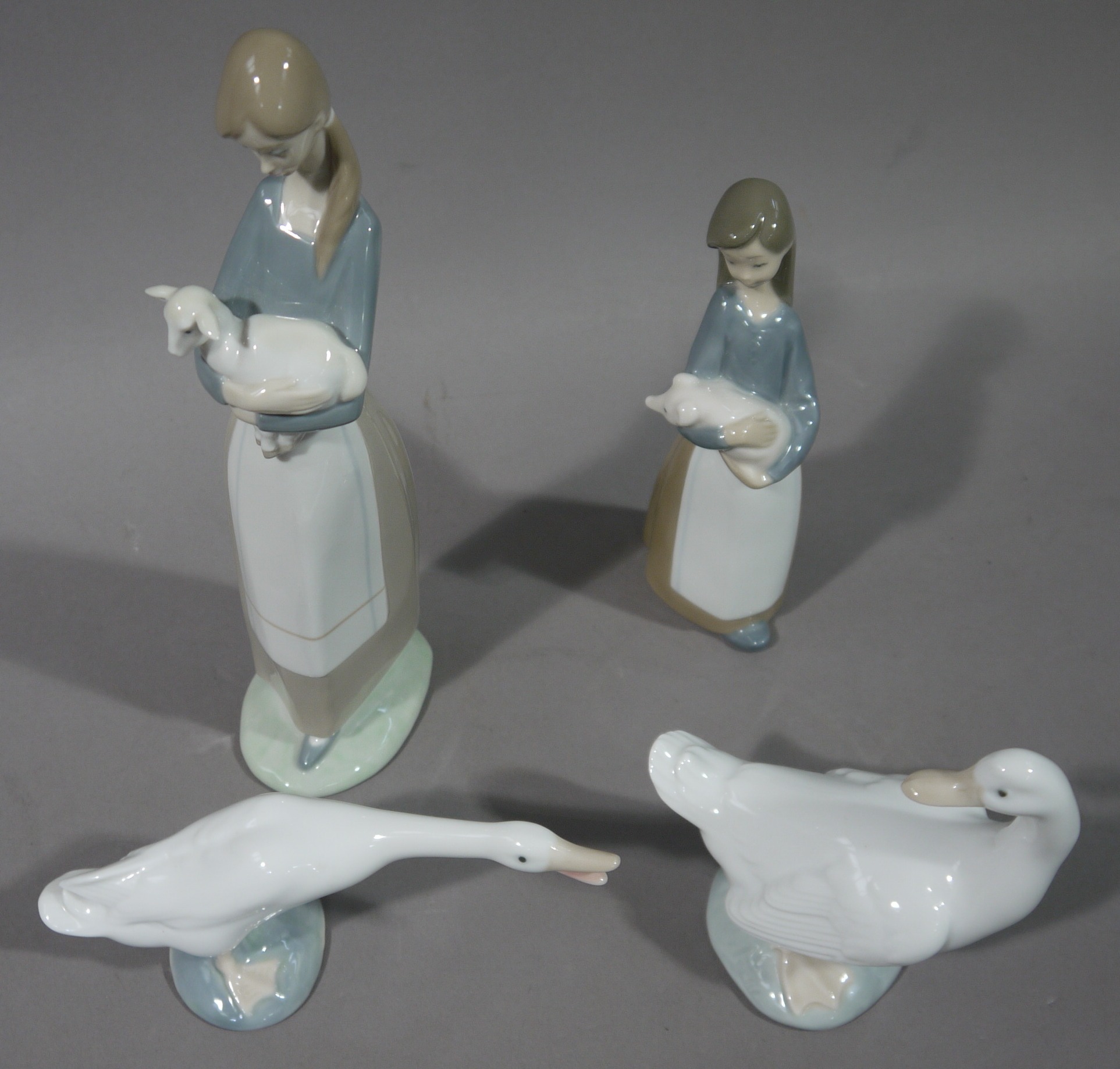 A Lladro country girl holding a lamb, another holding a piglet,