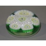 A glass paperweight of six flower heads in pale pink and white canes in green and clear glass,