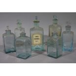 Seven pale blue tinted glass bottles of square outline with stoppers, various sizes,