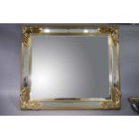 A large gilt framed wall mirror with mirrored panels to the margins and bold foliate moulded