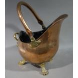 A copper and brass helmet coal scuttle on paw feet