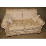 A two seater sofa upholstered in ivory damask fabric with scatter cushions