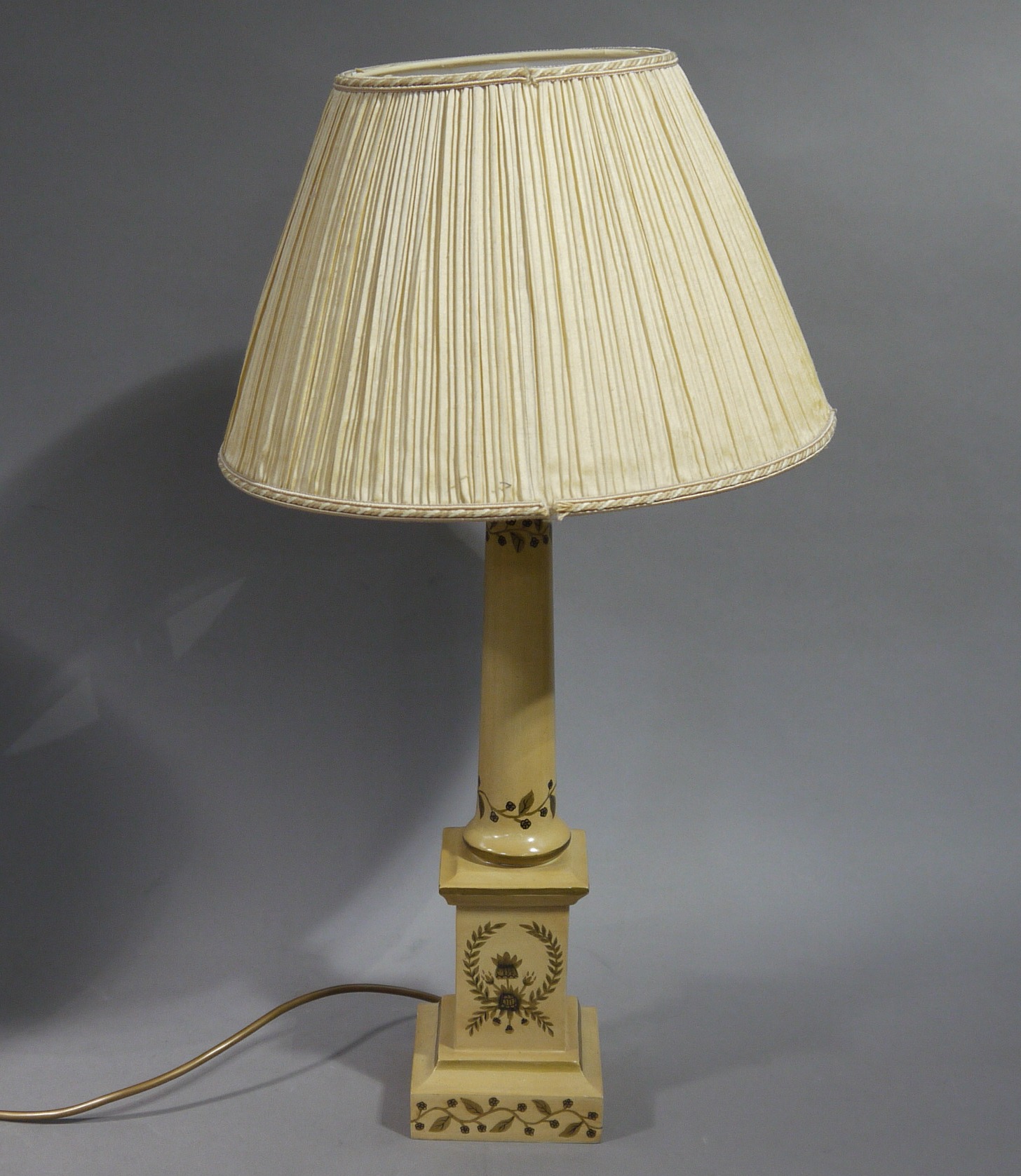 A metal table lamp decorated with floral trails and circlets with pleated cream shade
