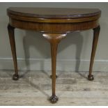 A mahogany demi lune foldover card table with foliate carved rim and on cabriole legs and on claw