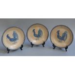 A set of three Italian pottery plates painted in underglazed blue with cockerels on a cream